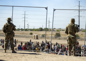 Migrantes esperan junto a una valla fronteriza mientras son vigilados por miembros de la Guardia Nacional de Texas. (Foto: AP/Andres Leighton)