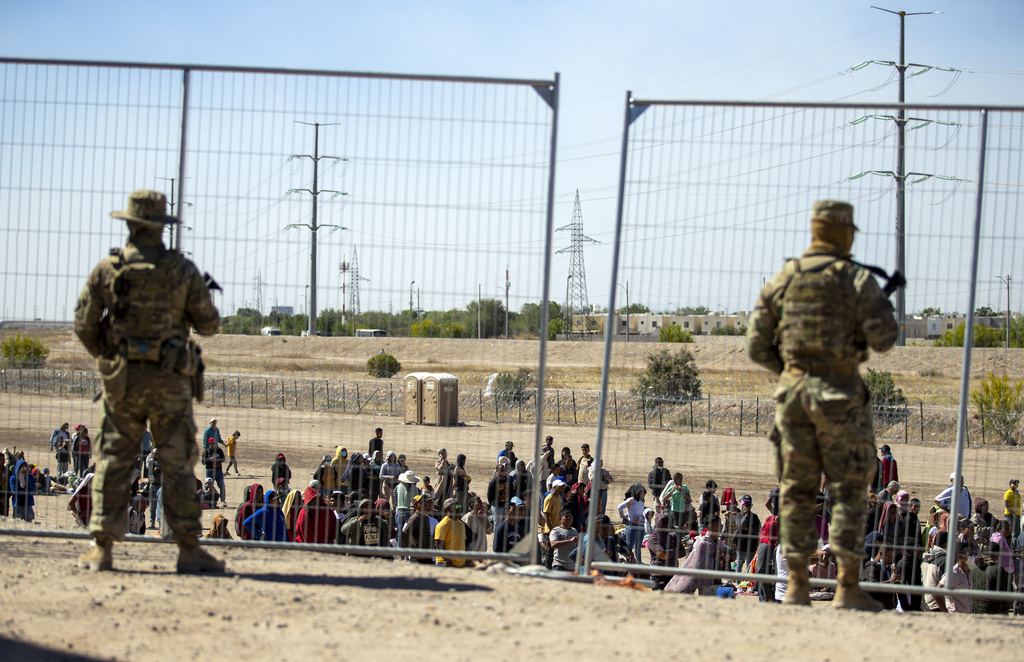 Migrantes esperan junto a una valla fronteriza mientras son vigilados por miembros de la Guardia Nacional de Texas. (Foto: AP/Andres Leighton)