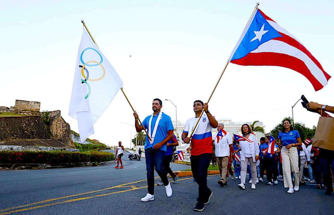 El abanderado para los Juegos Panamericanos Santiago 2023, Jean Pizarro, y el abanderado de los juegos anteriores, Franklin Gomez, caminan junto a los miembros de la delegación de Puerto Rico desde el Comité Olímpico hasta la Fortaleza. (Foto: Thais Llorca / EFE)