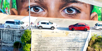 La obra acapara un muro de 185 pies de largo y 16 pies de alto, sobre el que se asoma un niño que parece mirar a la ciudad desde una ventana abierta en el monte. (Foto: Jonathan Hernández León)