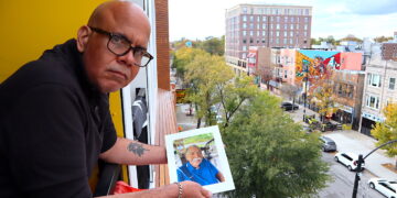 Elías Carmona Rivera sostiene la foto de su padre, Elías Carmona Alejandro, en el balcón de su apartamento en el barrio puertorriqueño de Chicago. Elías y su hermana Sandra son un ejemplo de los retos que enfrentan muchos hijos a cargo de cuidar a sus padres envejecidos, tanto en Puerto Rico como desde la diáspora. (Foto: Vanesa Baerga)