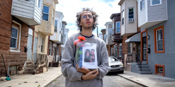 Guillermo Santos sostiene la urna con las cenizas de su padre en la calle, frente a la casa donde se crió en el barrio de Kensington, en Filadelfia. Su papá, nacido en Puerto Rico, murió de una sobredosis. (Foto: Solmaira Valerio / CPI)